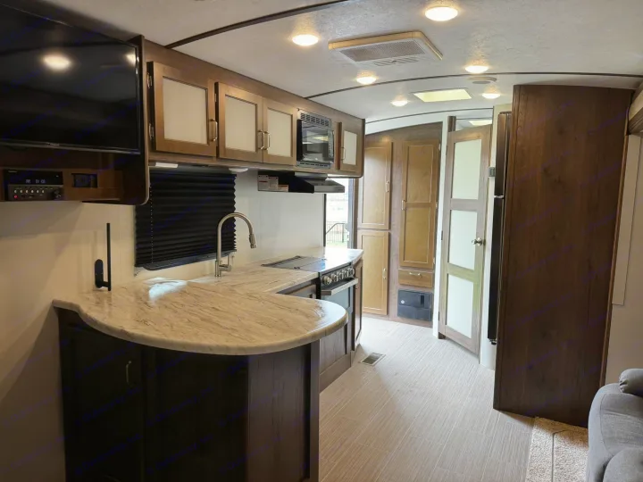Spacious RV rental kitchen with modern amenities, including a large counter, stove, microwave, and TV, showing a clean interior.. Keystone RV Passport Grand Touring 2019