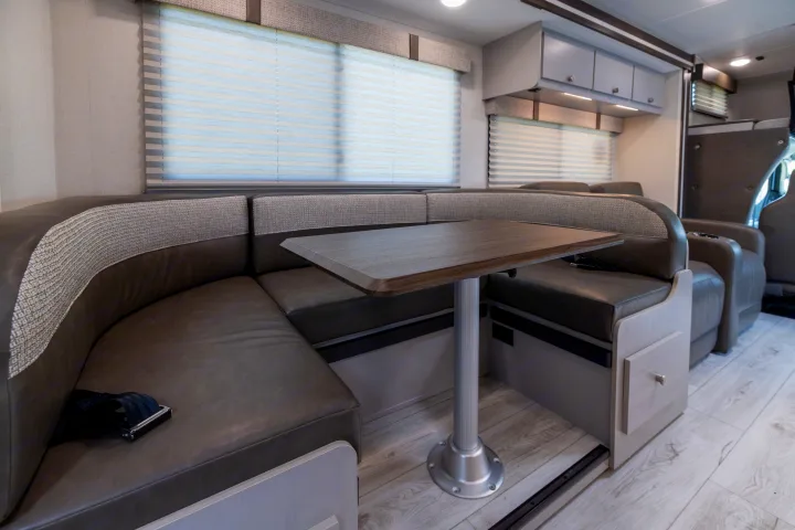 RV rental interior: U-shaped dinette with dark cushions, a wood table, and blinds. Perfect for dining & lounge space.. Coachmen Freelander 2027