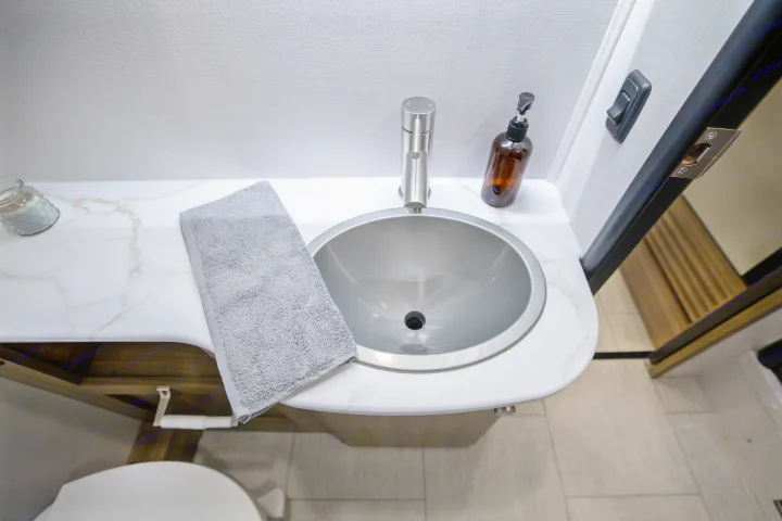 Modern RV rental bathroom sink area with a white marble-look counter, stainless steel sink, faucet, towel, and soap. Compact and functional.. Coachmen Freelander 2027