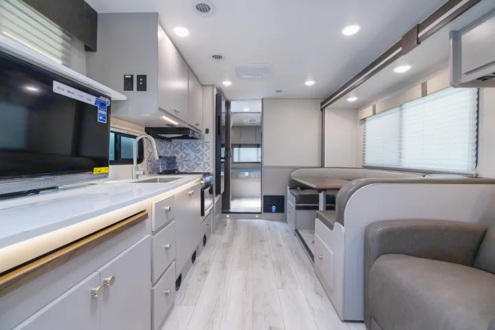 Modern RV rental interior featuring a bright kitchen with TV, and a spacious U-shaped dining area with comfortable bench seating.. Coachmen Freelander 2027