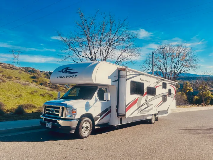 White Four Winds RV rental parked on a sunny road, featuring green hills, power lines, and a bright blue sky.. Thor Four Winds 2022
