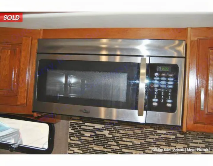 This RV kitchen features a stainless steel microwave oven, wood cabinets, and a mosaic backsplash, ready for your rv rental.. Holiday Rambler Endeavor 2018