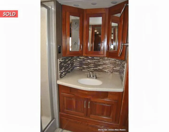 Explore this comfortable RV rental bathroom featuring a wood vanity, sink, mirrored cabinets, tiled backsplash, and an adjacent shower.. Holiday Rambler Endeavor 2018