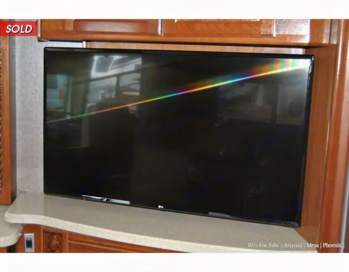 RV interior: TV with rainbow glare on screen, surrounded by wood cabinets & counter. Ideal entertainment for your rv rental.. Holiday Rambler Endeavor 2018