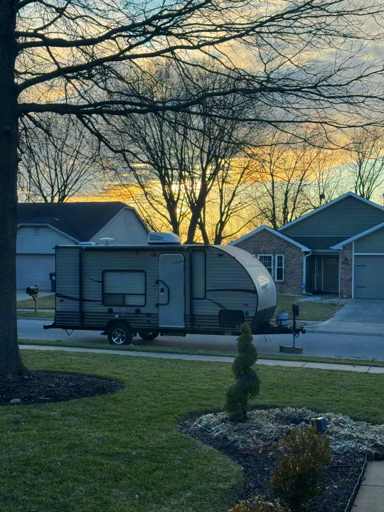 Gray travel trailer (RV rental) parked on a residential street at dawn/dusk, with bare trees and houses in the background.. Forest River Cherokee Wolf Pup 2016