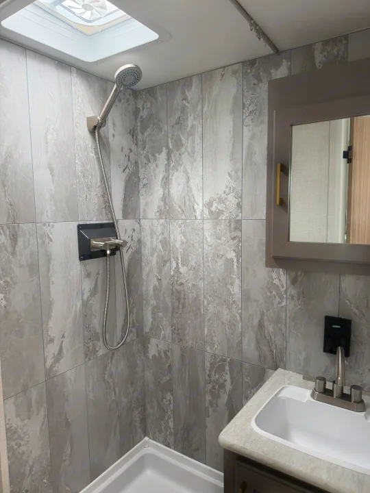 This RV rental's sleek bathroom boasts a grey tiled shower, handheld showerhead, vanity with sink, and mirrored cabinet.. KZ Sportsmen Classic 130BH 2026