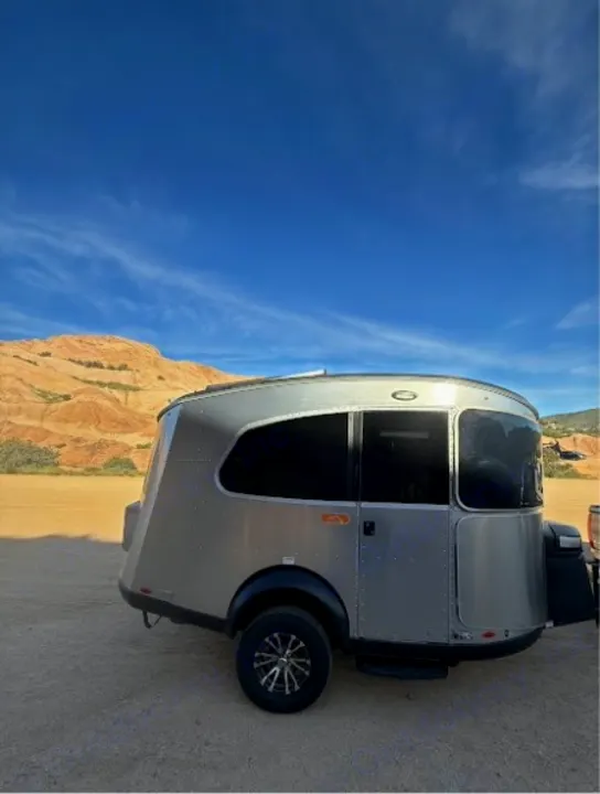 Experience adventure with this modern silver teardrop RV rental, a compact camper parked on dirt in a desert scene.. Airstream Basecamp 2020