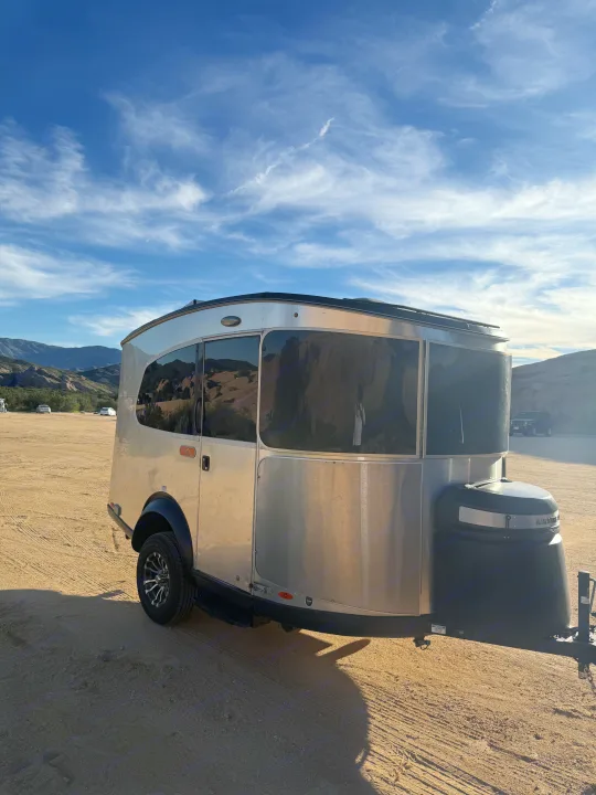 Airstream Basecamp rv rental: A silver travel trailer on a sandy lot, mountains in the background under a blue sky with wispy clouds.. Airstream Basecamp 2020