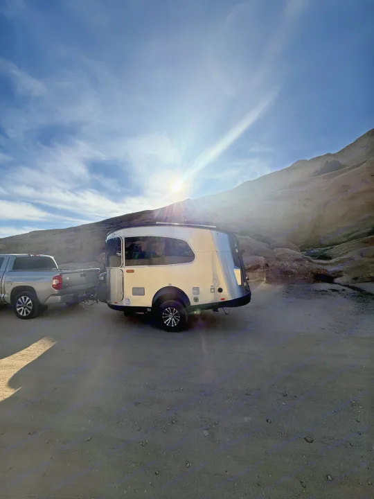 Your next RV rental journey starts here! Silver camper & truck parked in a sunny, rugged landscape with dramatic sun rays.. Airstream Basecamp 2020