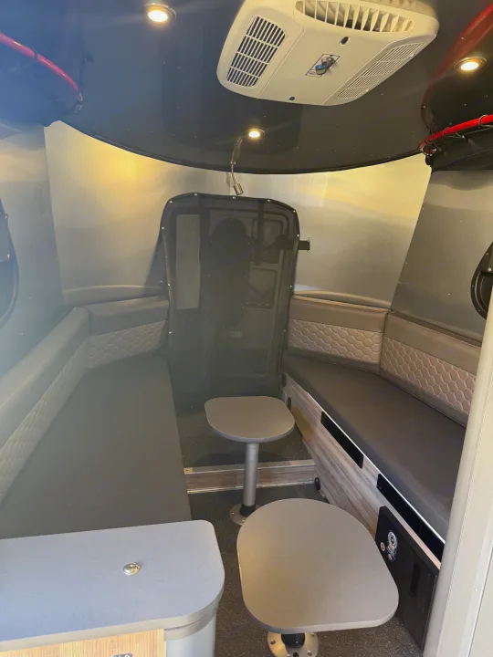 Explore this compact rv rental interior featuring a dinette with two tables, quilted bench seating, and an AC unit.. Airstream Basecamp 2020