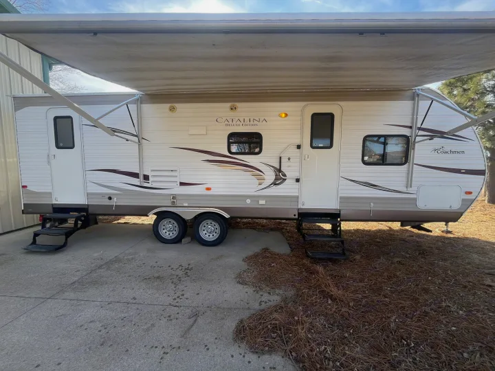 This white & brown Coachmen Catalina Deluxe Edition RV rental features an extended awning, two doors, and steps.. Coachmen Catilina Deluxe 2014