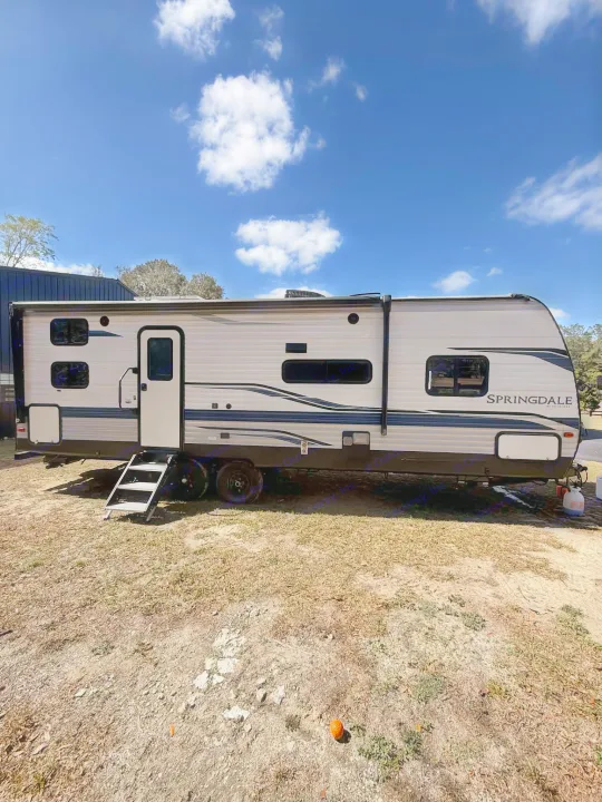 A large grey Springdale rv rental with steps down, parked on dry earth under a bright blue sky, ready for outdoor travel.. Keystone RV Springdale 2022