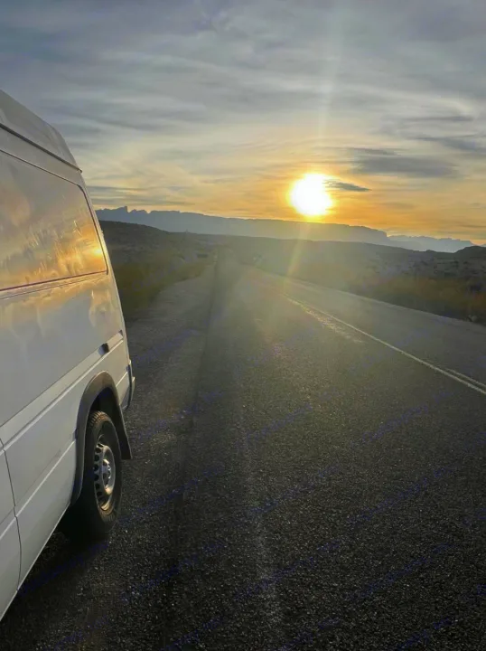 White RV rental van parked roadside, sun setting over distant mountains. Scenic road trip vibes.. Dodge Sprinter Van 2006