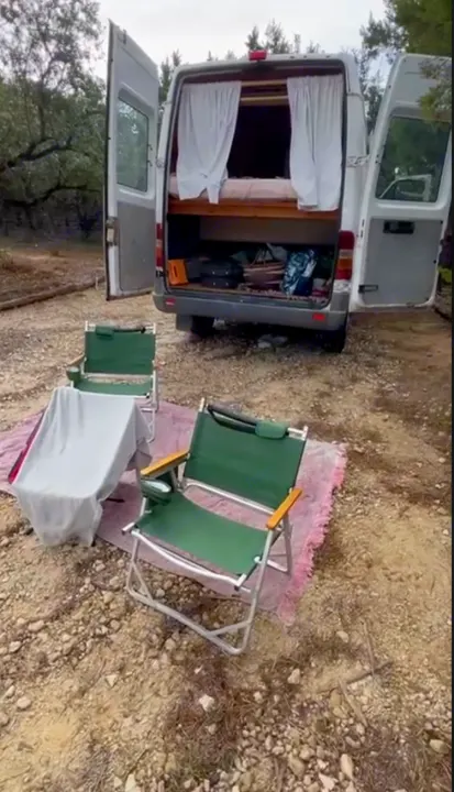 Cozy rv rental setup. Open camper van doors show a bed, storage. Two chairs on a rug invite outdoor relaxation.. Dodge Sprinter Van 2006