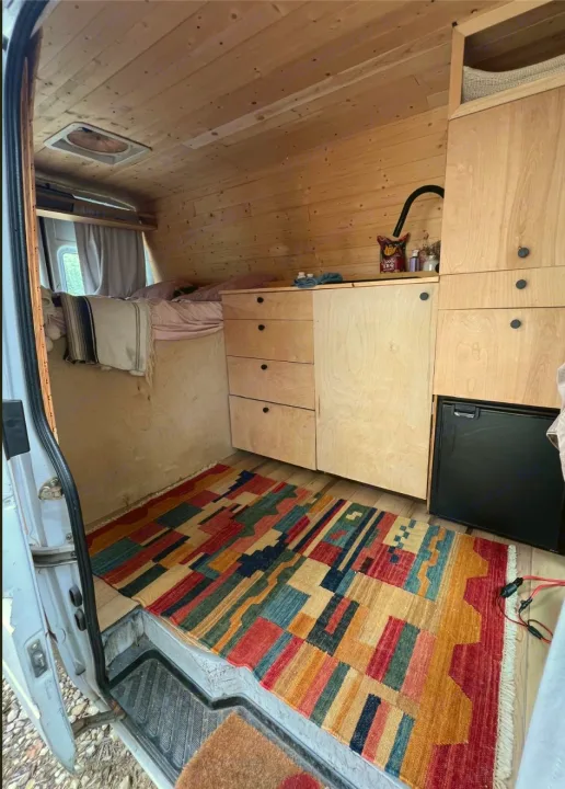 Cozy rv rental interior: wood-paneled camper van with bed, kitchen, fridge, and colorful rug. Ideal for mobile living.. Dodge Sprinter Van 2006