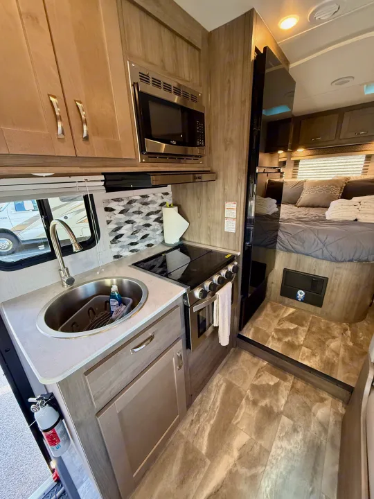 This RV rental offers a well-equipped kitchen with sink, stove, and microwave, plus a cozy bedroom visible from the living area.. Gulf Stream Conquest 2024