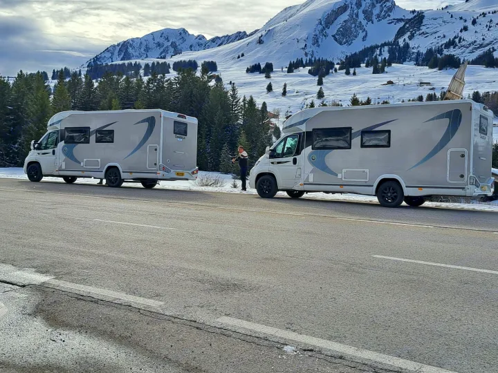 Two modern RV rental campervans parked on a winter mountain road with a person. Majestic snow-capped scenery.. Chausson 720 VIP Titanium 2021