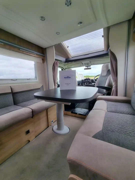 Spacious RV rental interior featuring a modern dining area, comfortable seating, and an information pack on the table.. Chausson 720 VIP Titanium 2021