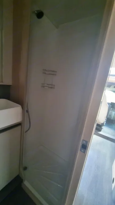 Compact shower and sink in an RV rental bathroom. Features a showerhead, storage caddy, and textured shower pan.. Auto-Trail F74 2025
