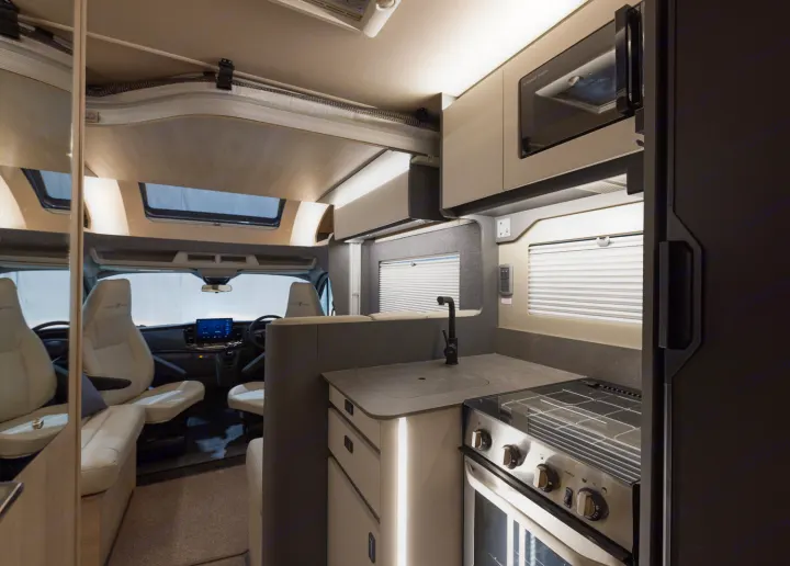 Inside a modern RV rental: sleek kitchen with oven, microwave, sink, comfy seating, and bright driver's area for your travels.. Auto-Trail F74 2025