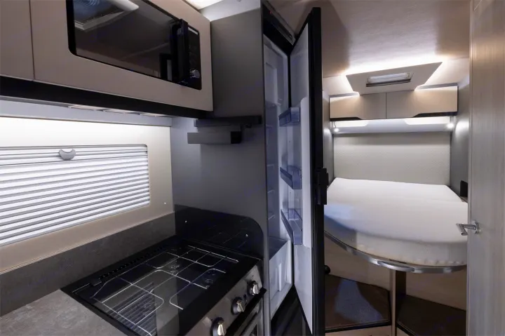 Compact rv rental interior featuring a kitchenette, open fridge, and comfortable convertible bed.. Auto-Trail F74 2025