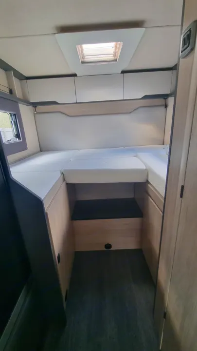 RV rental interior: A compact sleeping area with white mattresses, overhead cabinets, a small window, and a ceiling skylight.. Auto-Trail F70 2025