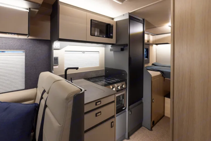 Modern RV rental interior with a compact kitchen (stove, microwave, fridge), seating, and bedroom. Perfect for adventure travel.. Auto-Trail F70 2025
