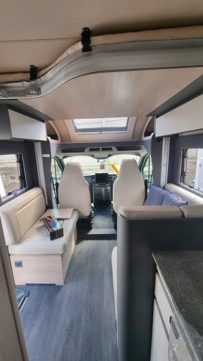 RV rental interior: spacious campervan looking forward, with front cab, comfortable seating, kitchen, and overhead bed.. Auto-Trail F70 2025