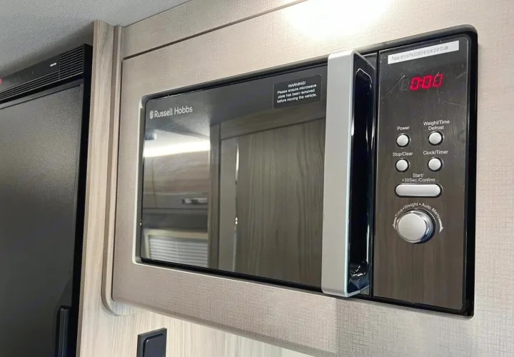 Built-in Russell Hobbs microwave in an RV rental, showing safety warnings for travel. Adjacent to a refrigerator.. Elddis CV80 2024
