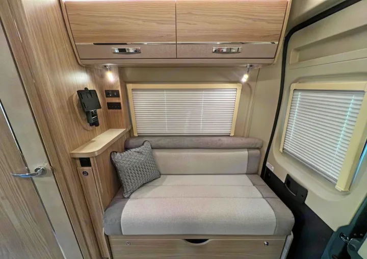 This RV rental interior showcases a modern, light-toned living space with a sofa that converts to a bed, overhead storage, and blinds.. Elddis CV80 2024