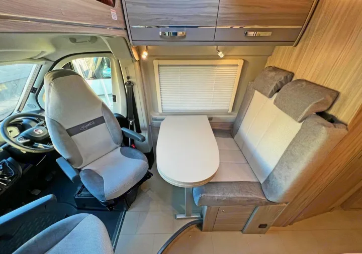 Spacious RV rental interior: swivel driver's seat, dining table, cozy bench seating, and overhead storage for comfortable travel.. Elddis CV80 2024