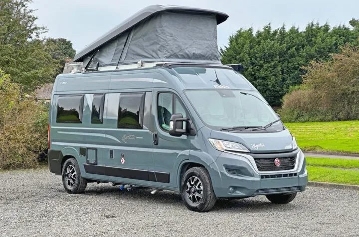 Modern gray pop-top camper van, perfect for RV rental, parked on gravel with green surroundings.. Elddis CV80 2024