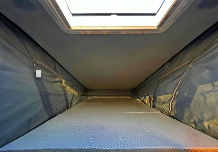 Interior of an rv rental pop-top camper, showing the cozy sleeping area with a mattress, fabric walls, and skylight.. Elddis CV80 2024