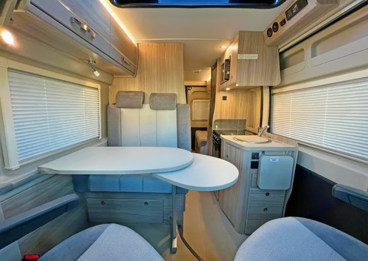 Bright rv rental interior: dinette table, kitchen with sink & stove, overhead storage, and blinds for comfy trips.. Elddis CV80 2024