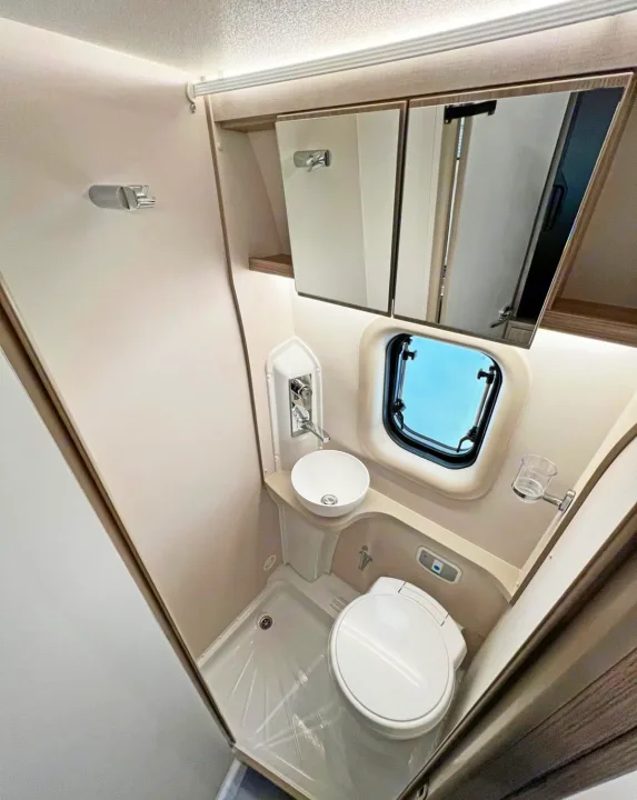 This bright, compact RV rental bathroom features a toilet, small sink, shower area, and storage mirrors.. Elddis CV80 2024