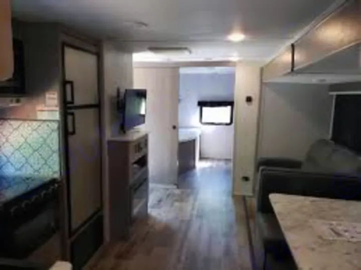 RV rental interior: kitchen, living area with sofa & TV, and hallway leading to bedroom. Bright, modern travel trailer.. Dutchmen Coleman Light 2023