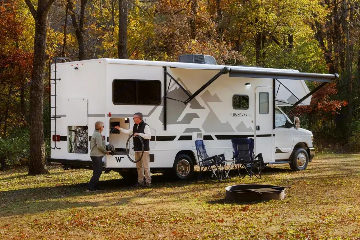 An RV rental with an extended awning & gear storage. A couple preps bikes at their scenic fall campsite, ready for adventure.. Winnebago Sunflyer 24GG 2027