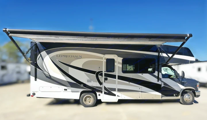 Sleek Coachmen Leprechaun RV rental with a deployed awning, featuring black, white, and gray graphics, parked under a clear sky.. Coachmen Leprechaun 2020