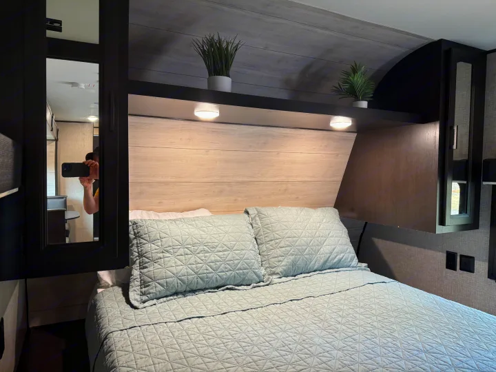Cozy RV rental bedroom features a comfy bed with quilted bedding, a modern headboard with reading lights, and decorative plants.. Jayco Jay Flight 2022