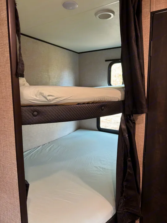 Comfortable RV rental bunk beds with privacy curtains and windows, perfect for family sleeping in a compact camper interior.. Jayco Jay Flight 2022