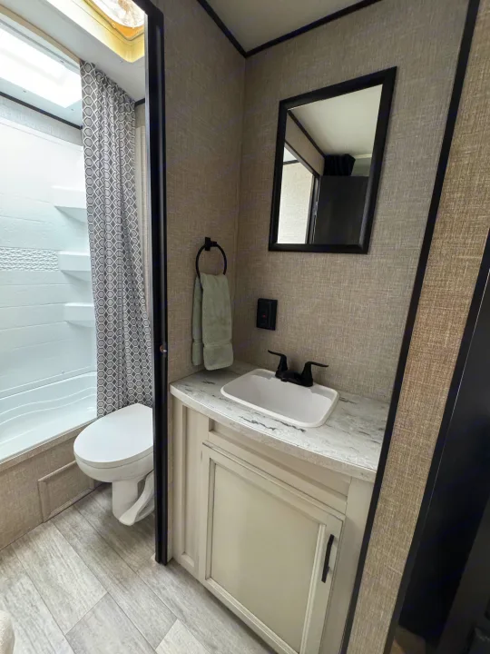 Modern RV rental bathroom: shower, toilet, vanity with sink, mirror. Light paneling walls & wood-look floor for comfort.. Jayco Jay Flight 2022