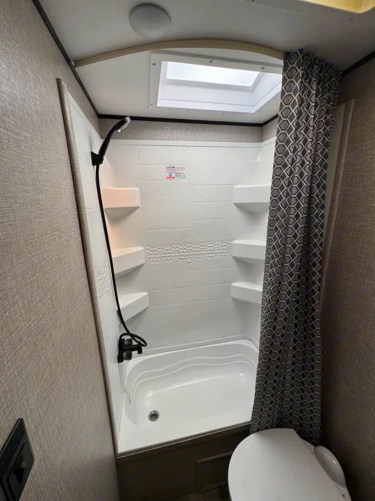 RV rental bathroom featuring a white shower with built-in corner shelves, a geometric patterned shower curtain, and skylight.. Jayco Jay Flight 2022