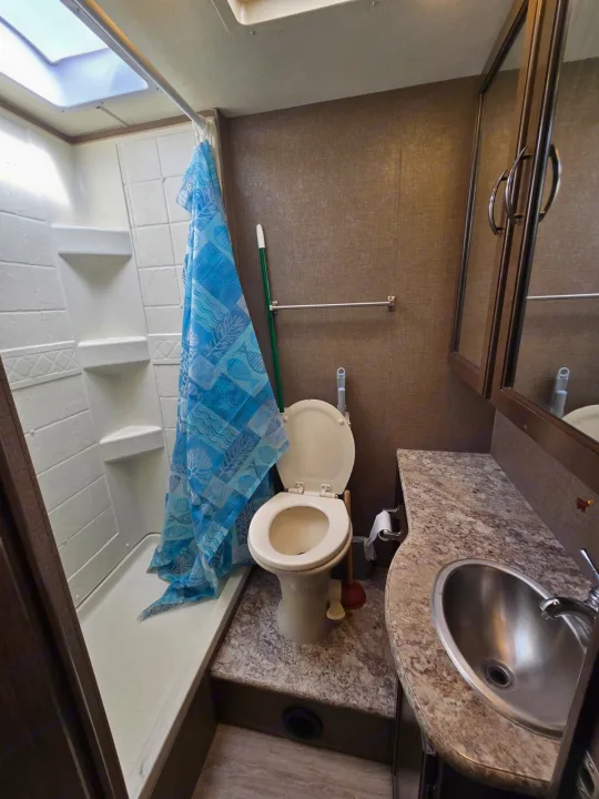 Compact RV rental bathroom with a shower, blue curtain, toilet, and sink area. Ideal for travel accommodation.. Thor Four Winds 2019