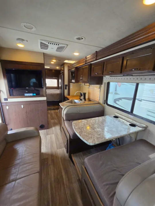 Spacious RV rental interior with living, dining, and kitchen areas. Features a sofa, dinette, mounted TV, and bedroom for comfortable travel.. Thor Four Winds 2019