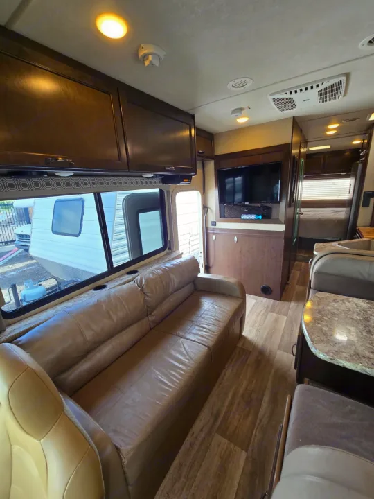 Cozy RV rental interior featuring a beige sofa, dining booth, flat-screen TV, and a glimpse into the bedroom.. Thor Four Winds 2019