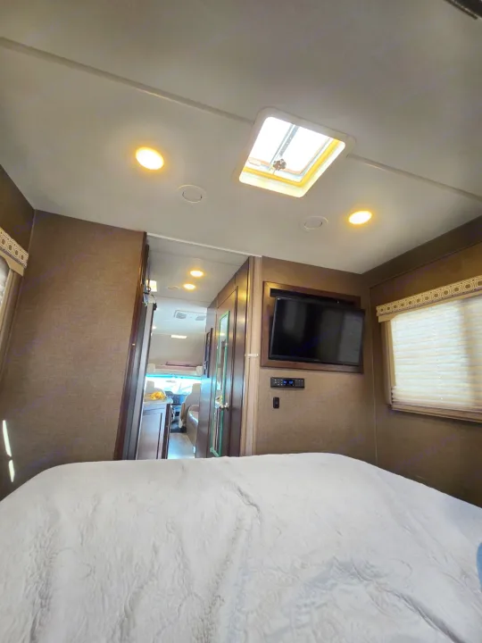 An inviting RV rental bedroom with a comfy bed, mounted TV, ceiling skylight, and a clear path to the front.. Thor Four Winds 2019