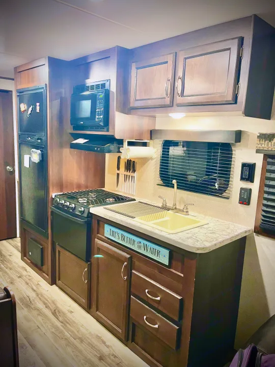 Well-equipped RV rental kitchen featuring a fridge, microwave, gas stove, sink, and wood cabinetry. Perfect for travel adventures.. Jayco Jay Flight SLX 2018