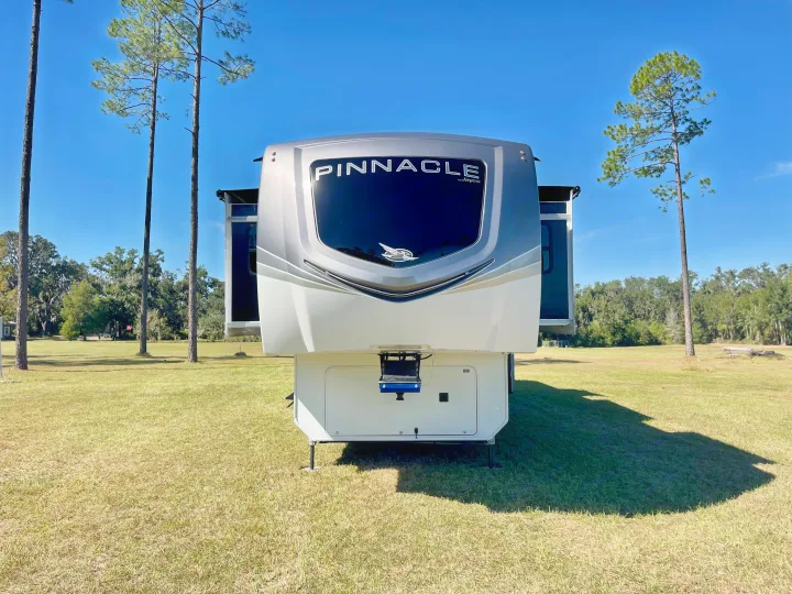 Pinnacle by Jayco fifth-wheel RV rental parked in a sunny field with pine trees, ready for your next camping adventure.. Jayco Pinnacle 2023