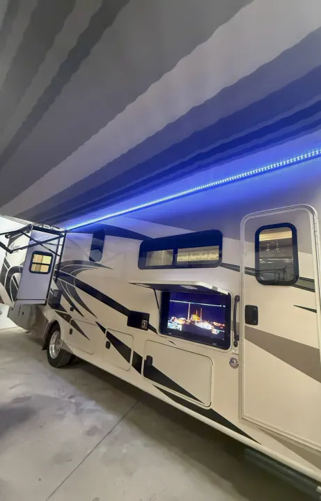 Spacious RV rental with an extended awning illuminated by blue LED lights and an outdoor TV displaying a night scene.. Coachmen Encore 2021