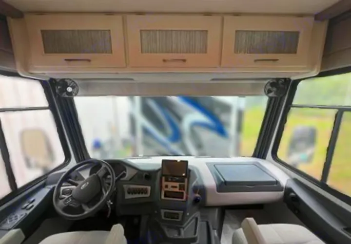 RV rental cockpit featuring steering wheel, dashboard, overhead cabinets, and side fans. Blurred view through windshield.. Coachmen Encore 2021